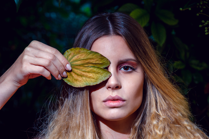 modelo curbriendose un ojo con una hoja de arbol